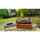 A basket of dark chocolate squares tied with twine sits on a stone surface outdoors, with a blurred garden background.