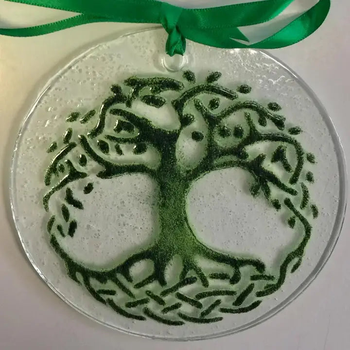 Decorative glass ornament with tree of life design and green ribbon on a white background