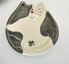 Ceramic plate shaped like a cat's face with gray and white design on a white background