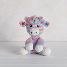 Crocheted highland cow toy with multicolored mane on a white wooden surface