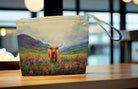 Pouch with a painting of a highland cow in a field on a wooden surface.