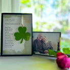 Framed photo of an elderly couple with a green shamrock and text on a table with a blurred outdoor background.