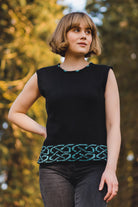 Woman wearing a black sleeveless top with green pattern in a forest setting