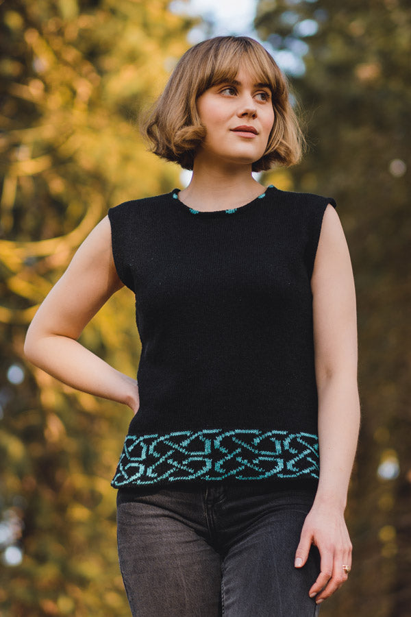 Woman wearing a black sleeveless top with green pattern in a forest setting