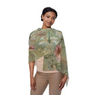 A woman modeling a lightweight draped wrap or shawl with a botanical print in muted sage green, dusty pink, and beige tones, paired with a beige top and tan pants against a plain white background.