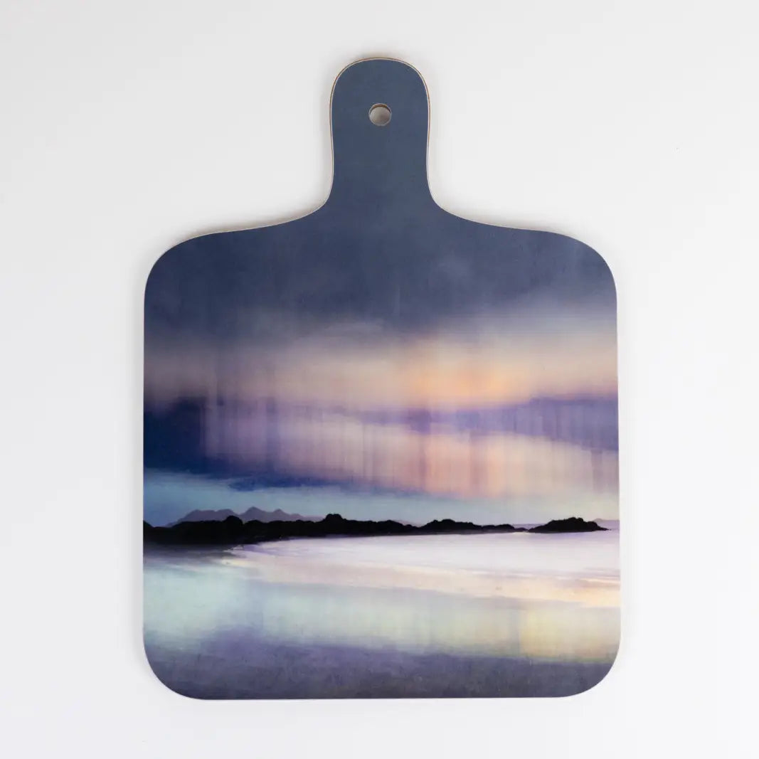 A wooden cutting board with a handle, featuring a printed abstract landscape design of a lake or sea with mountains and a sunset sky in shades of blue, purple, and orange, shown against a plain white background.