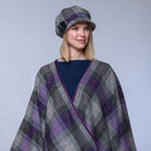 Woman wearing a plaid cape and hat against a gray background