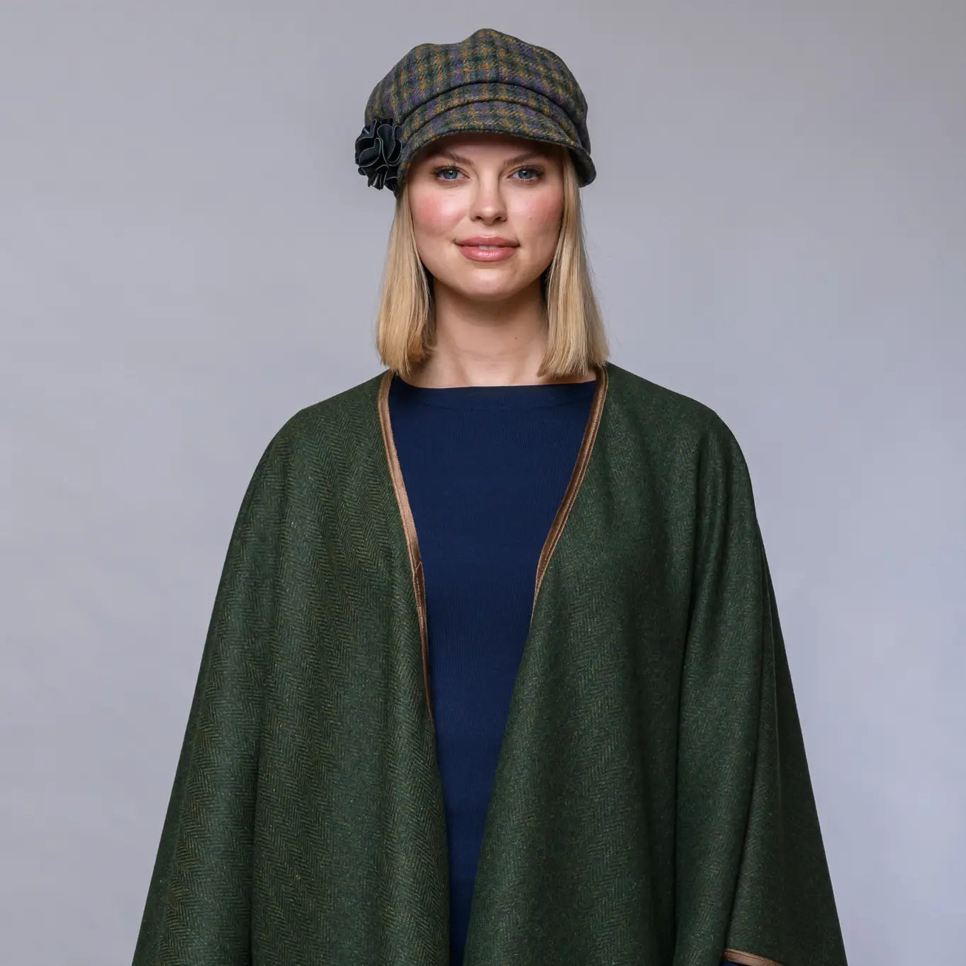 Woman wearing a green cape and plaid hat against a gray background