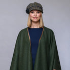 Woman wearing a green cape and plaid hat against a gray background