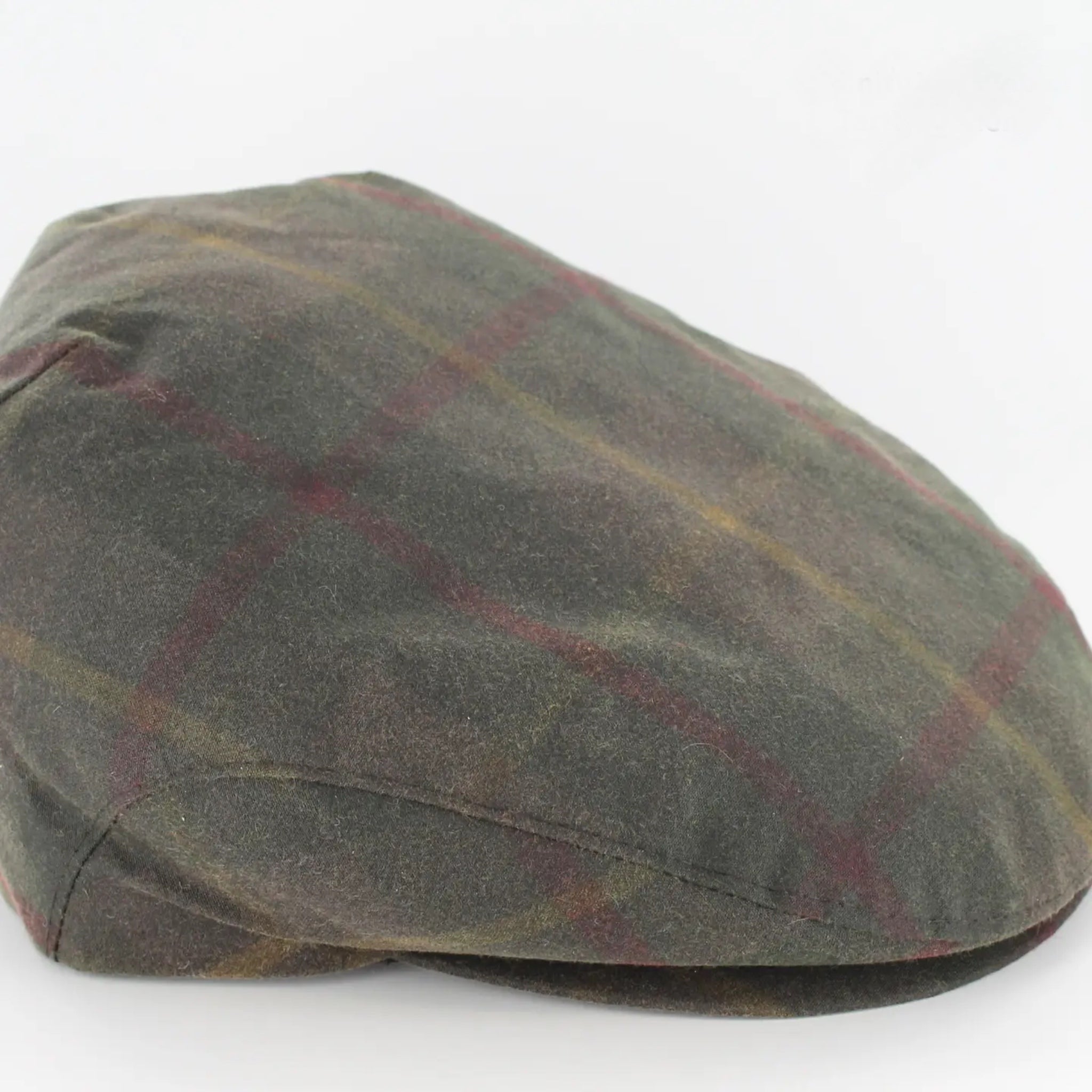 A flat cap made of textured wool in a muted olive green color, featuring a subtle plaid pattern with thin red and yellow lines, photographed on a white background.