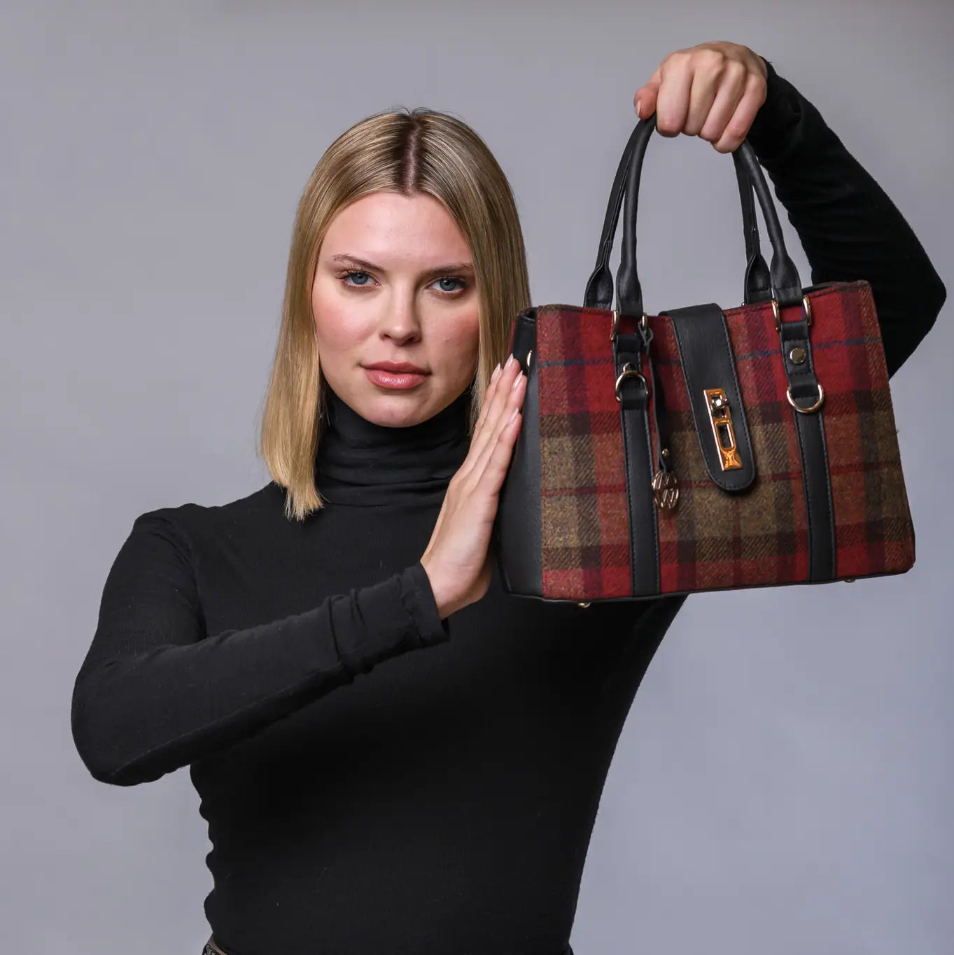 Woman holding a red and black plaid handbag against a gray background