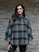 Woman wearing a plaid poncho against a stone wall background