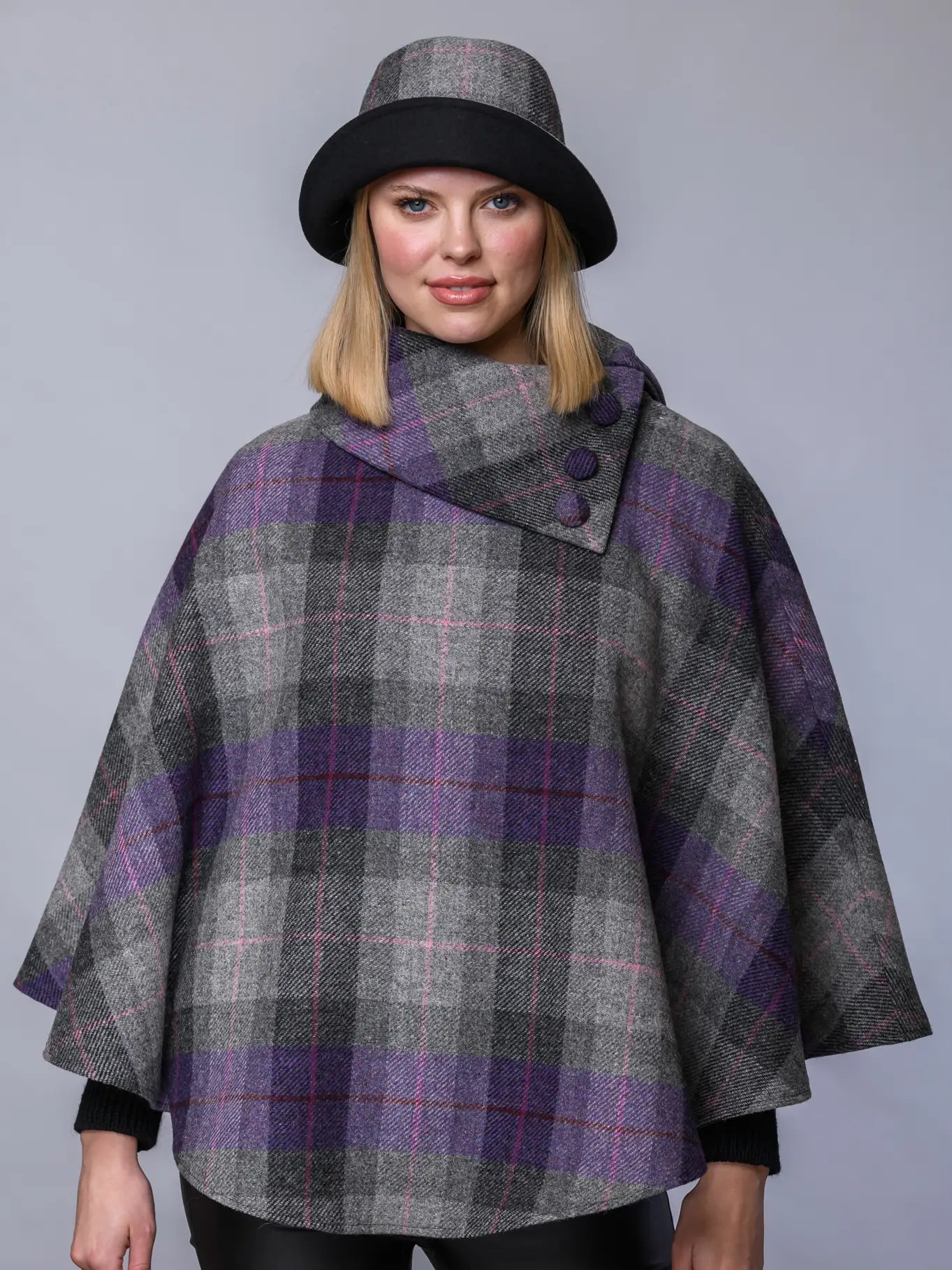 Woman wearing a gray and purple plaid cape with a matching hat on a gray background