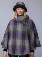 Woman wearing a gray and purple plaid cape with a matching hat on a gray background