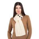 Woman wearing a beige sweater and cream scarf with black buttons on a white background