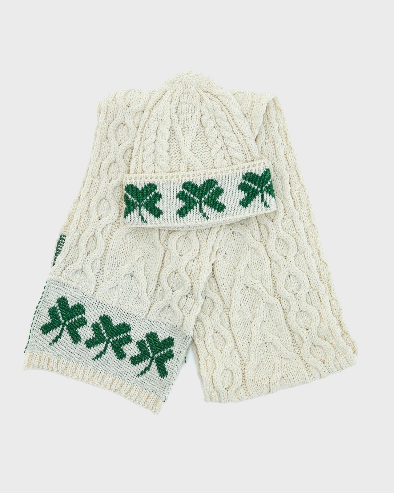 Cream-colored cable knit scarf with green shamrock pattern on a white background