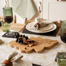 Dining table setting with a wooden cutting board, glasses, and plates.