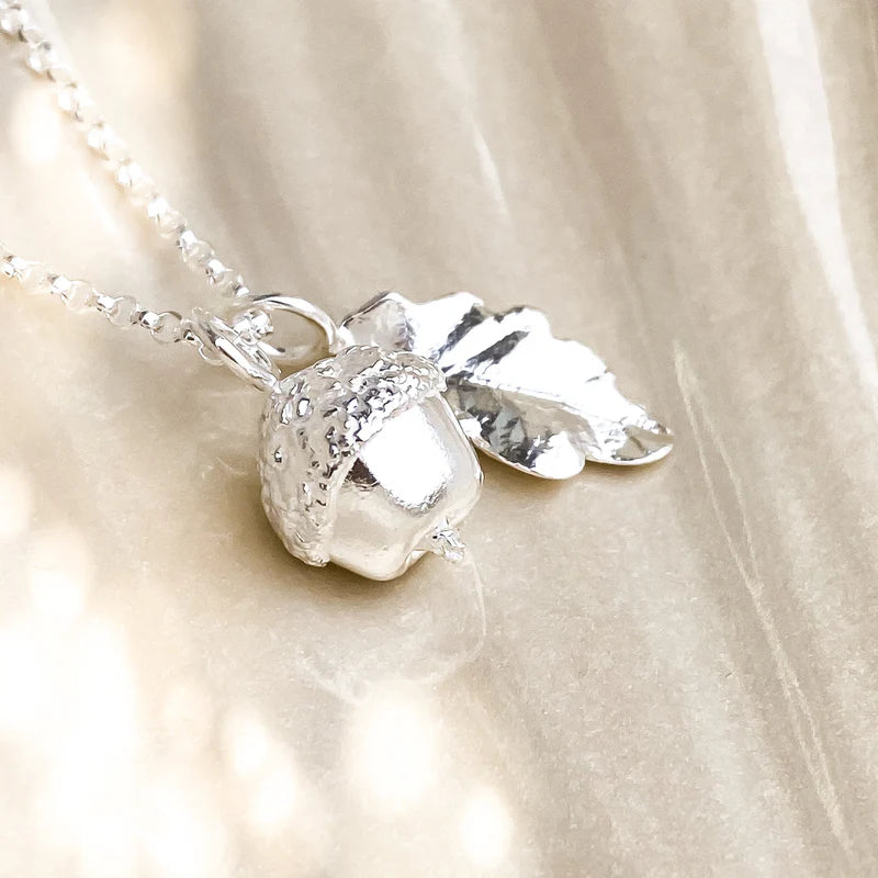 Silver acorn and leaf pendant necklace on a beige fabric background
