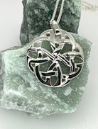 Silver Celtic knot pendant on a chain, displayed on a piece of green stone.