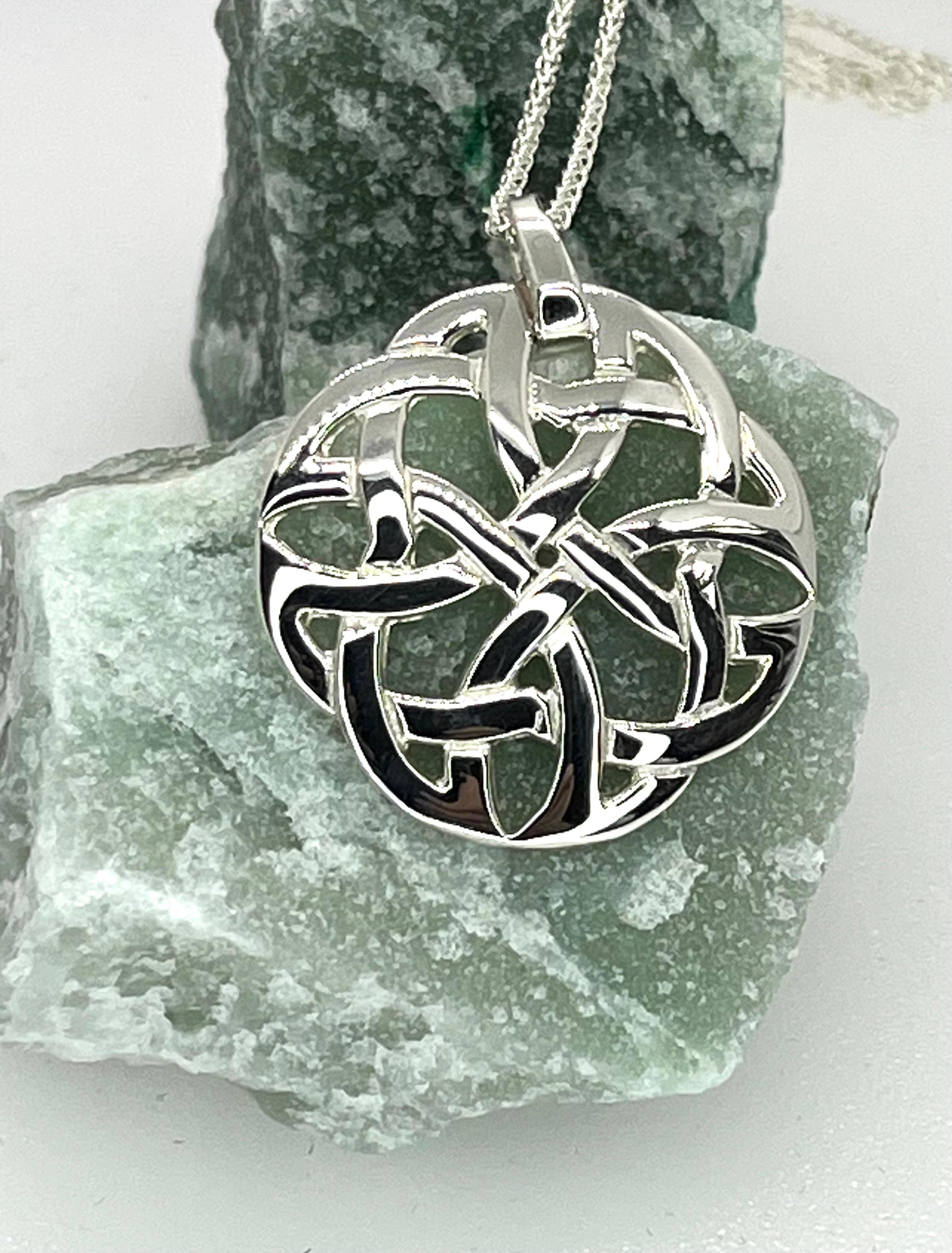 Silver Celtic knot pendant on a chain, displayed on a piece of green stone.