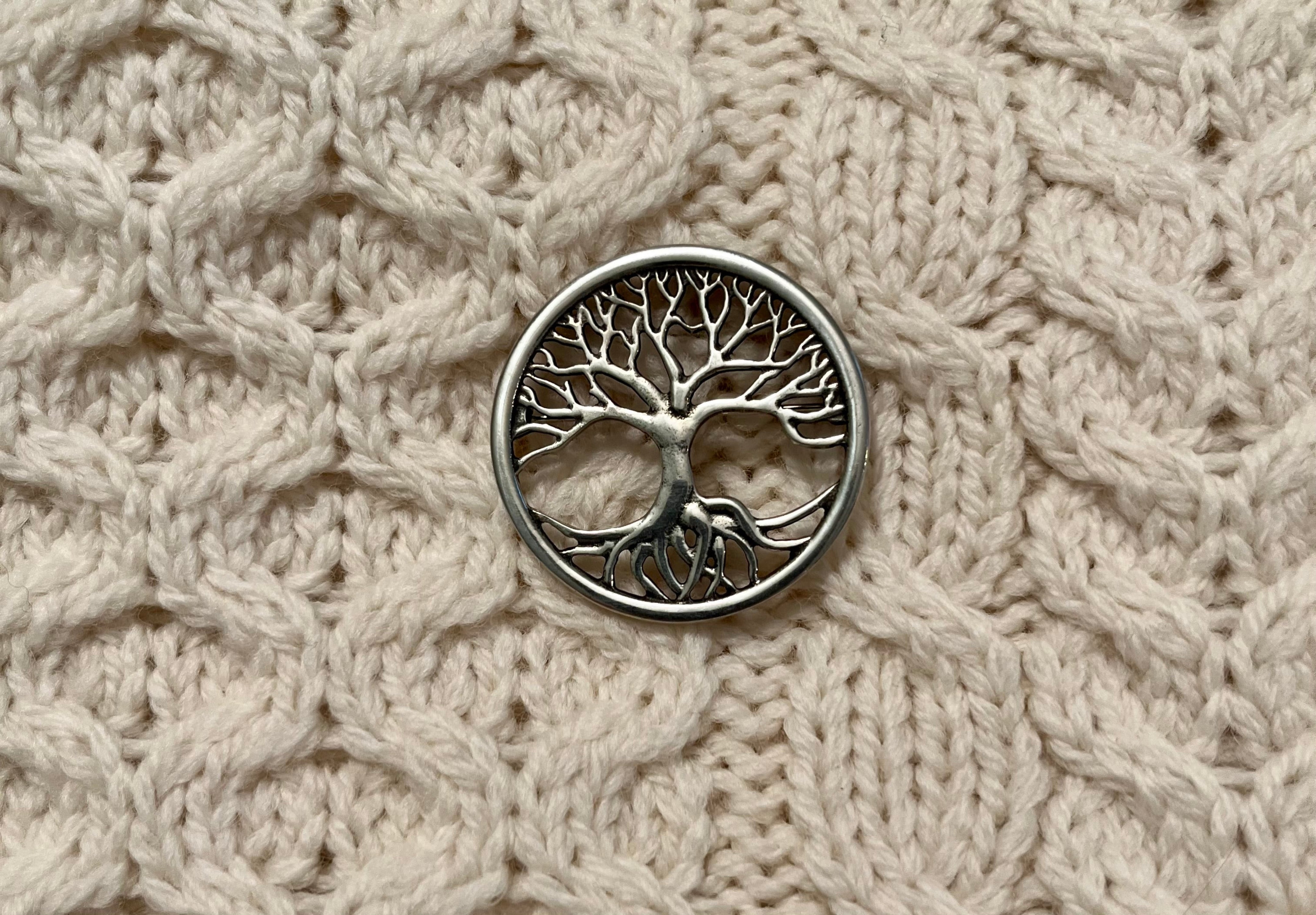 Silver tree of life brooch on a textured beige fabric background