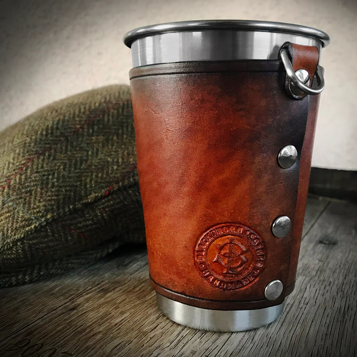Leather-covered cup with metal top and bottom on a wooden surface