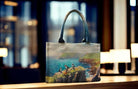 Tote bag with a scenic design of puffin on a rock by a body of water, placed on a surface with a blurred background.