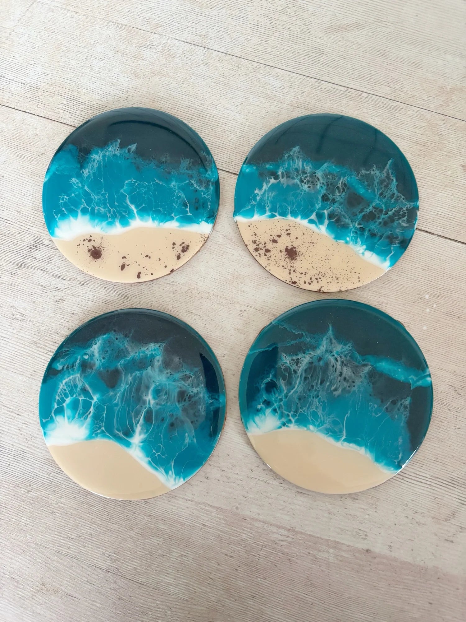 Four coasters with a beachscape design featuring blue ocean waves and beige sand on a light wooden surface.