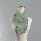 A lightweight square scarf with a dragonfly and floral print in muted sage green, blue, and gold, displayed on a white mannequin torso against a solid gray background.