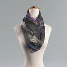 A draped scarf with a dark gray and black geode or amethyst crystal pattern, featuring purple and blue accents, displayed on a white mannequin torso against a neutral gray background.