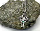 Silver cross pendant with a green gemstone on a stone surface