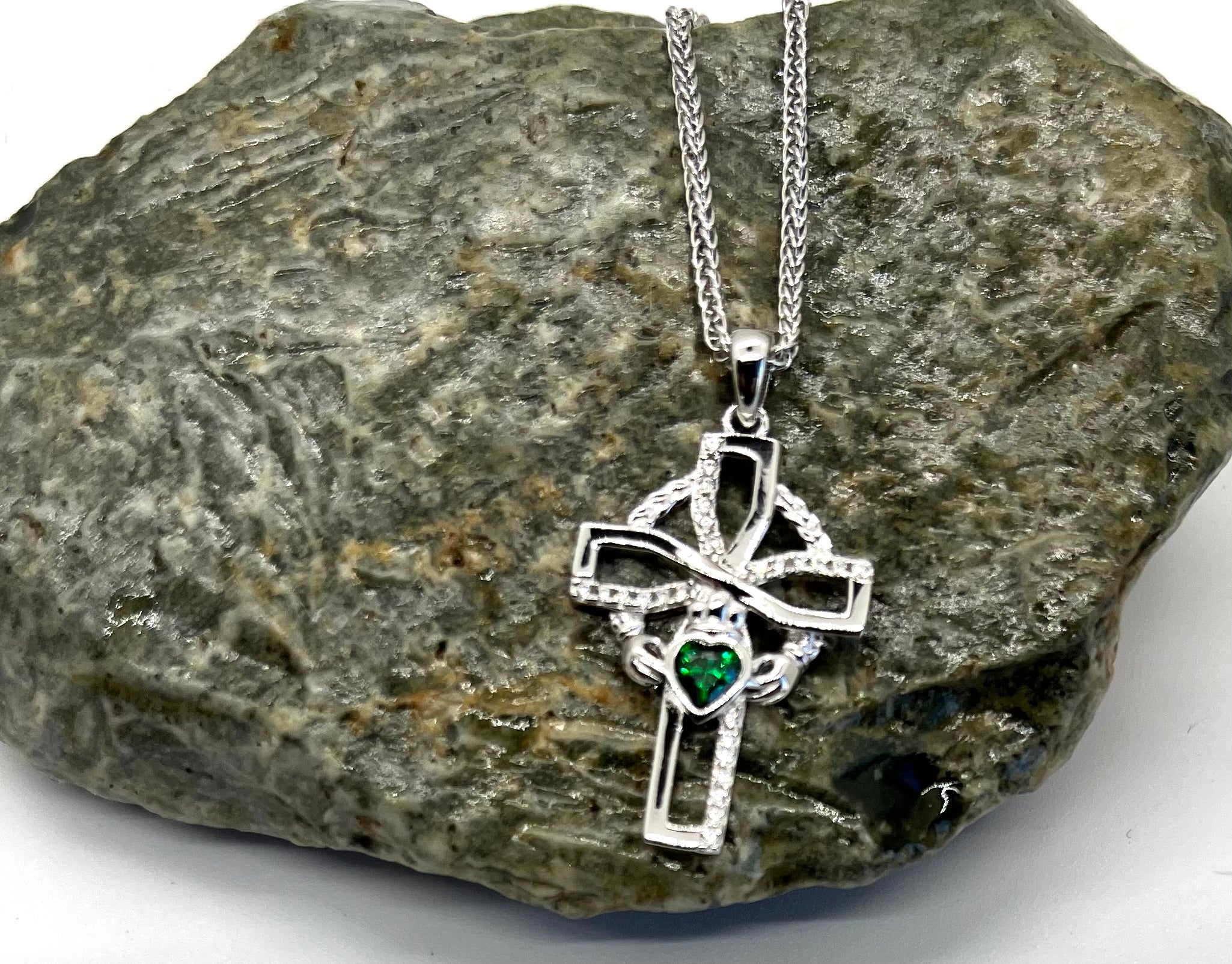 Silver cross pendant with a green gemstone on a stone surface