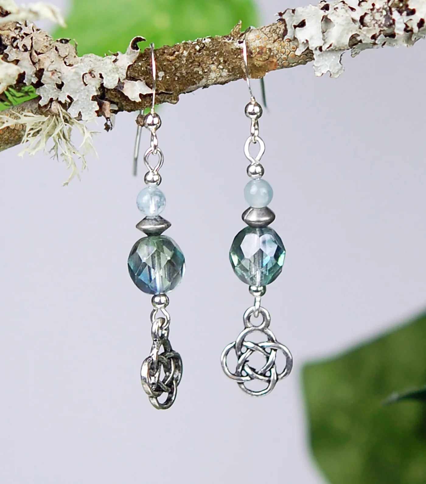 Pair of earrings with blue beads and silver Celtic knot design hanging from a branch.
