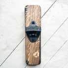 A rustic wall-mounted bottle opener featuring a rectangular stained wood block with a black metal blade. The blade is embossed with the brand name 'BLAINDE' and is mounted on a white-painted wooden plank background.