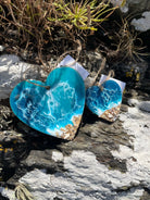 Two turquoise heart-shaped stones on a rocky surface with plants.