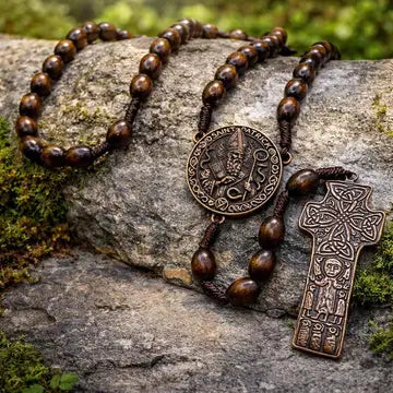 A wooden and metal religious rosary with a round medallion and a cross pendant, displayed on a mossy rock outdoors.