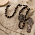 A dark brown wooden bead rosary with a round medallion and a cross pendant, displayed on a textured beige linen fabric.