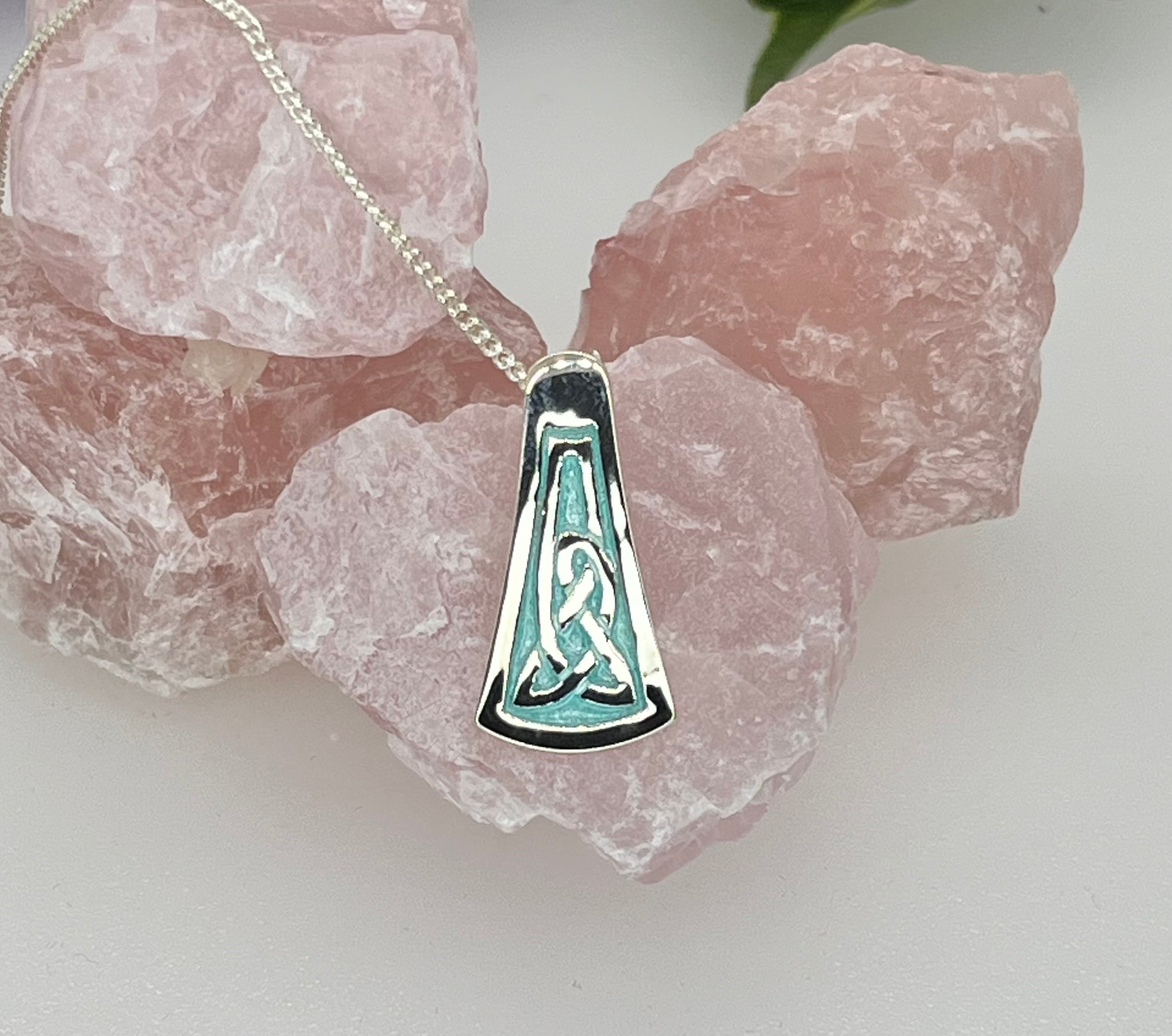 Silver pendant with green enameled design on a chain, set against pink crystal stones.