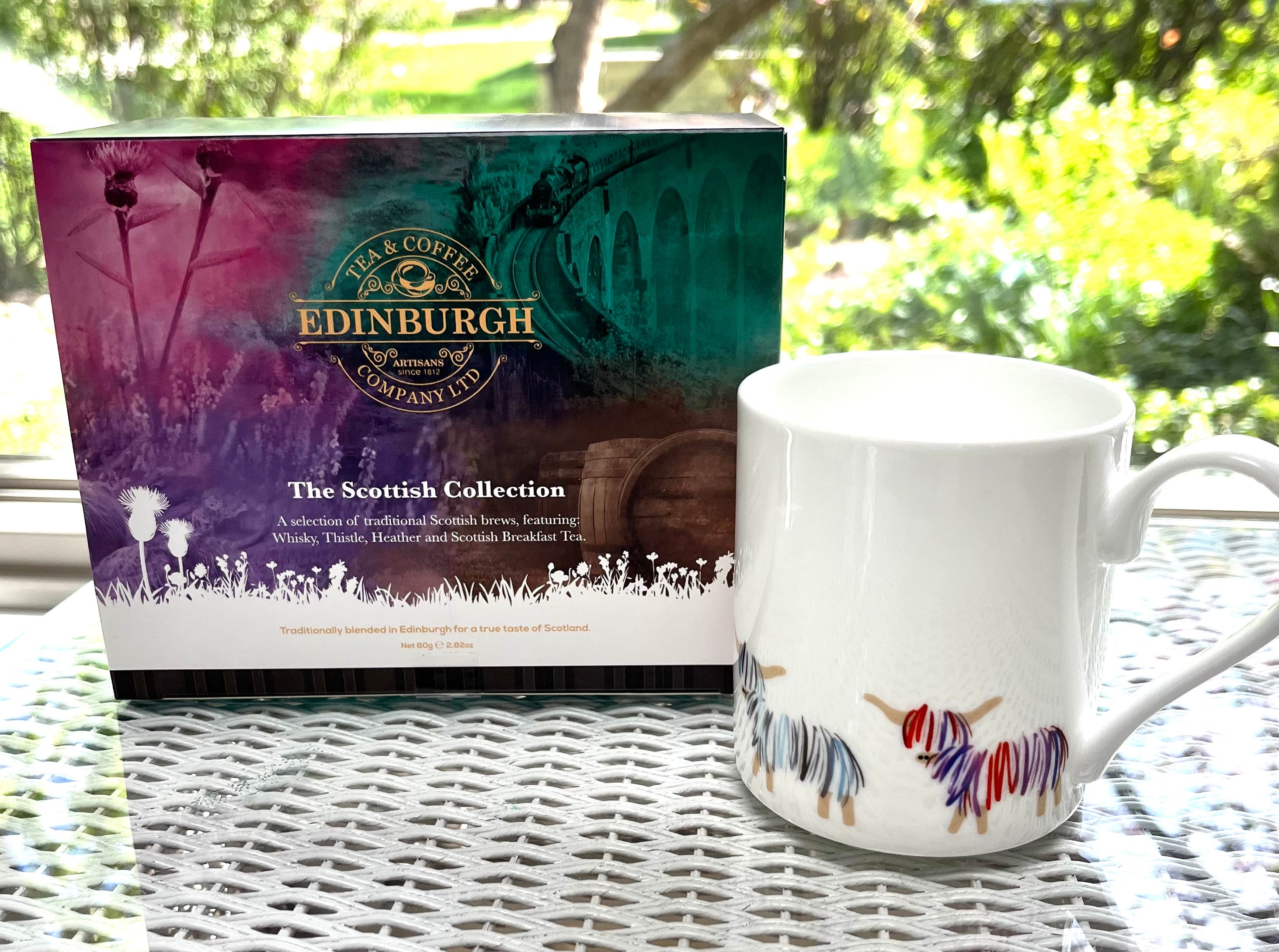 Edinburgh Tea & Coffee Company box and mug with yarn design on a wicker table outdoors.