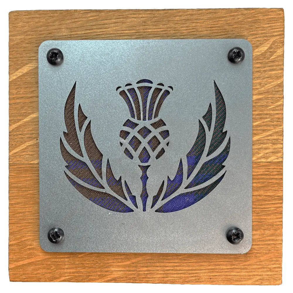 A square metal plaque featuring a laser-cut thistle and laurel design, mounted on a square wooden board with four visible black screws.