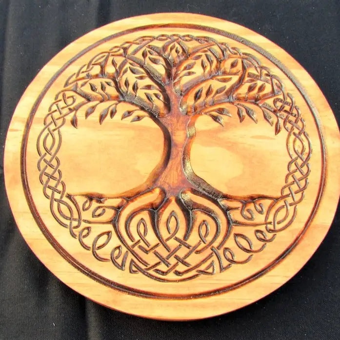 A round wooden plaque featuring a carved Celtic-style tree of life with roots and branches integrated into an interlaced knot border, shown on a black background.