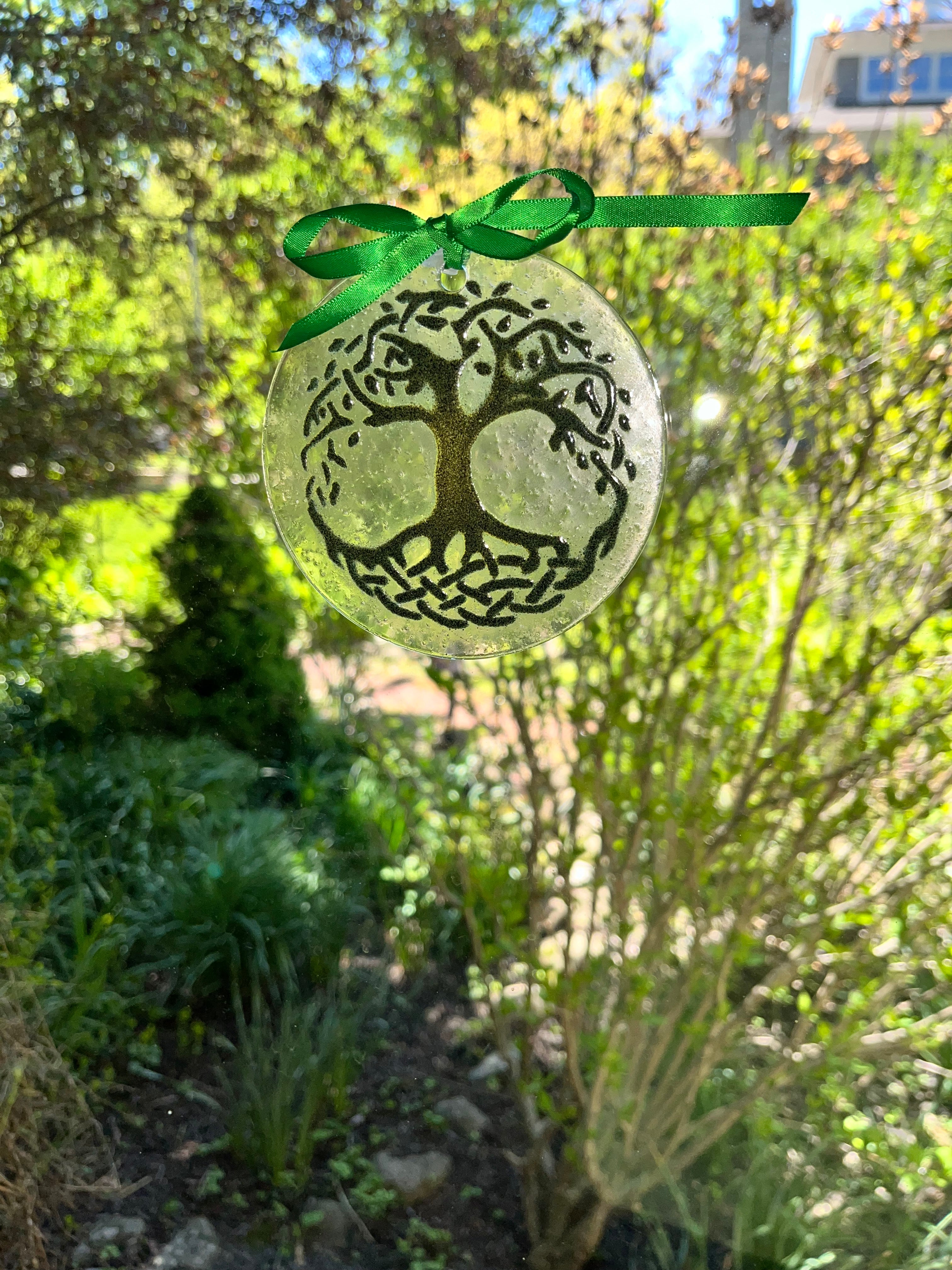Decorative ornament with tree design on a green ribbon against a natural background