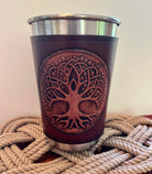 Brown leather cup with tree design on a metal base, placed on a woven surface.