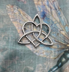 A silver-toned metal Celtic triquetra knot pin or brooch, displayed on a textured, blue-toned fabric background.