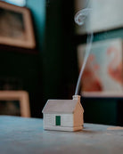 Small house-shaped incense burner with smoke emerging on a table.