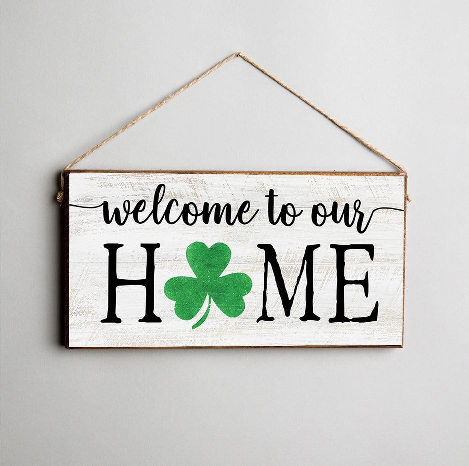Wooden sign with 'welcome to our HOME' text and a green clover on a gray background