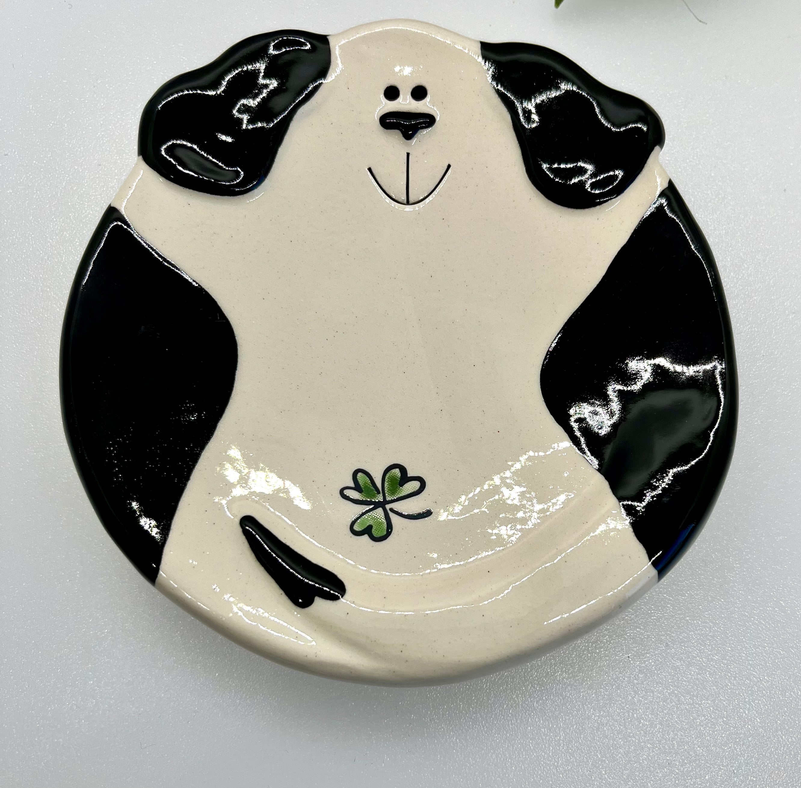 Ceramic plate shaped like a black and white dog face with a clover on a white background