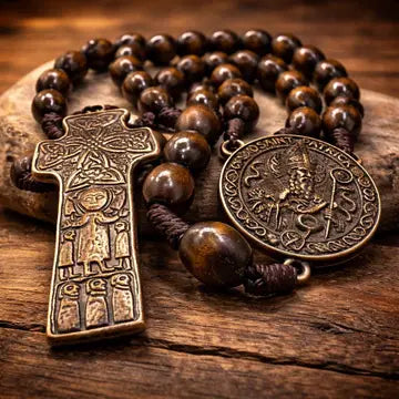 A close-up of a wooden bead rosary with an antique bronze cross pendant and a round medallion, resting on a rustic wooden surface.